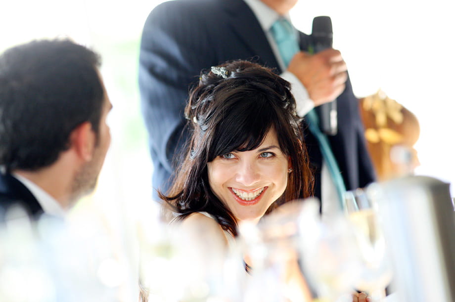 Bride smiling during a wedding speech by Martin Beddall Photography