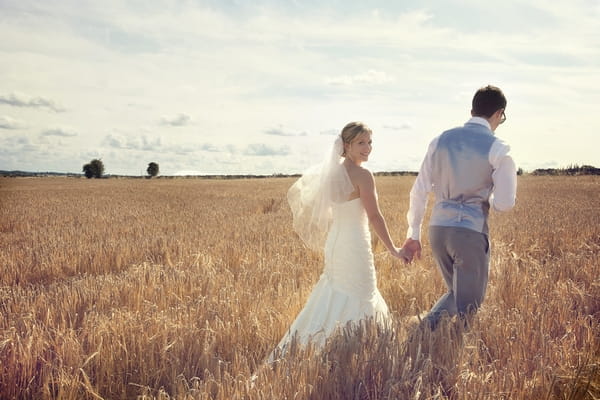 Bride and groom walking through corn fields - Picture by Chasing Moments Photography