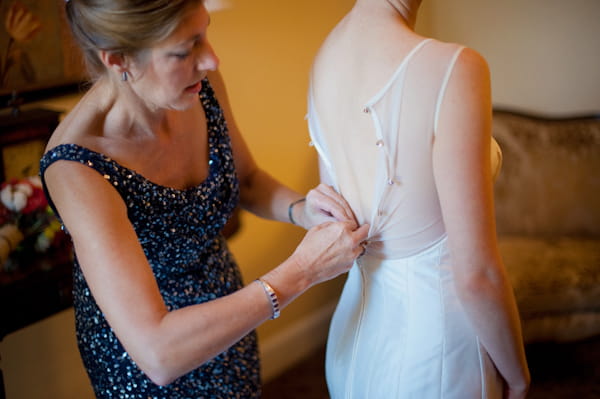 Bride having back of wedding dress done up for her - Picture by Rojo Foto Design