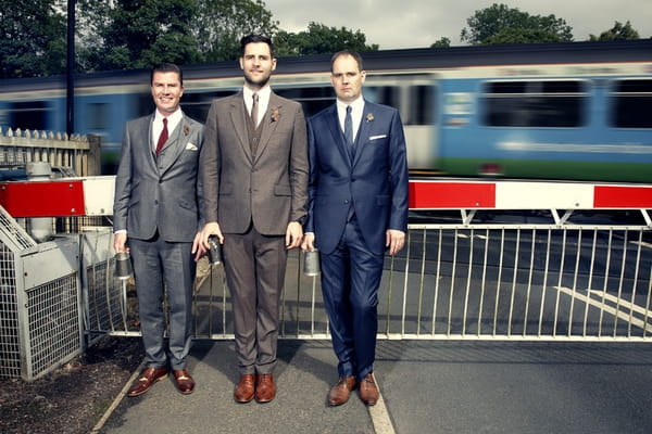 Groomsmen standing in front of railway as train goes past - Picture by Ian Shoots Weddings