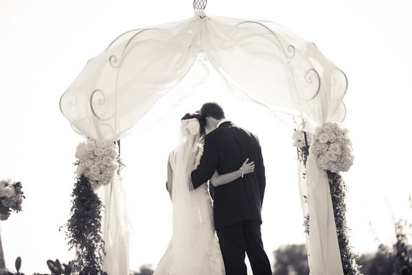 Bride and groom under arch at wedding ceremony - Picture by Allyson Magda Photography