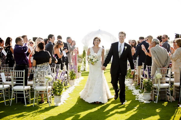 Bride and groom walking out of ceremony holding hands - Picture by Allyson Magda Photography