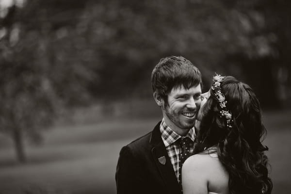 Groom smiling as bride kisses him on the cheek - Picture by Jonas Peterson Photography