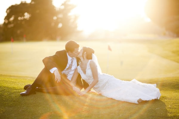 Bride and groom sitting on golf course - Picture by Allyson Magda Photography