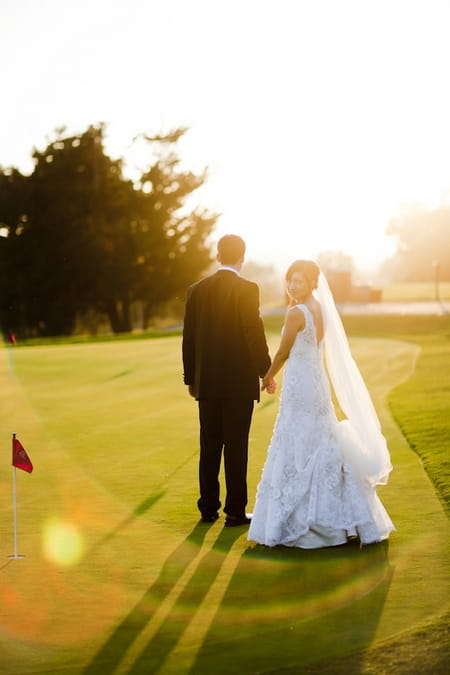 Bride and groom holding hands on golf course - Picture by Allyson Magda Photography