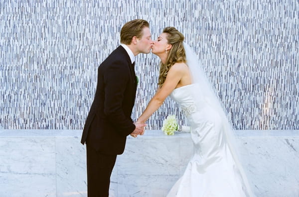 Bride and groom kissing in front of mosaic wall - Picture by Yvette Roman Photography