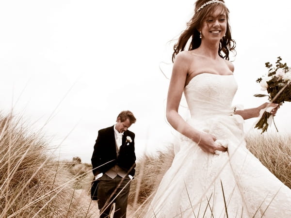 Bride and groom walking through long grass - Picture by Archibald Photography