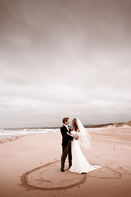 Bride and groom standing on heart in the sand on beach - Picture by Archibald Photography