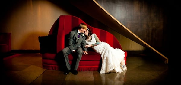 Bride and groom on red sofa - Picture by John Charlton Photography