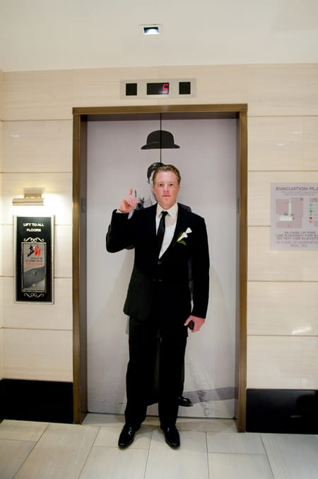 Groom standing in front of a lift with picture of hat above his head - Picture by Yvette Roman Photography