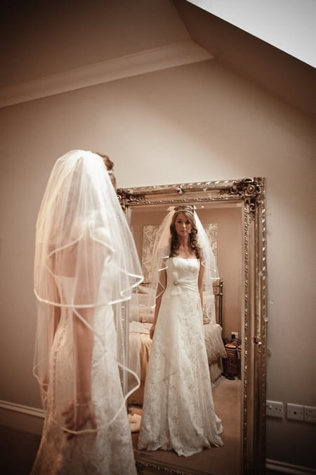 Bride looking at her reflection in mirror - Picture by Archibald Photography
