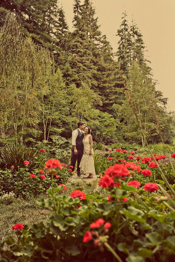 Vintage bride and groom standing amongst red flowers - Picture by Paco and Betty