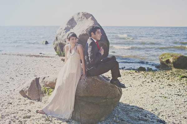 Bride and groom sitting on rock on beach - Picture by Our Labor of Love Photography