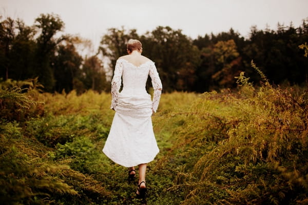 Bride in lace wedding dress walking across field - Picture by Judy Pak Photography
