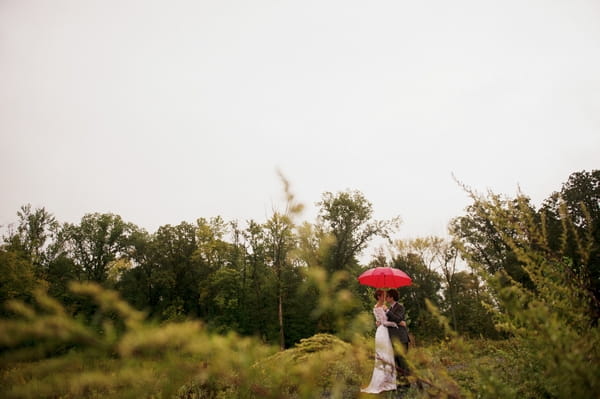 Bride and groom in field with red umbrella - Picture by Judy Pak Photography