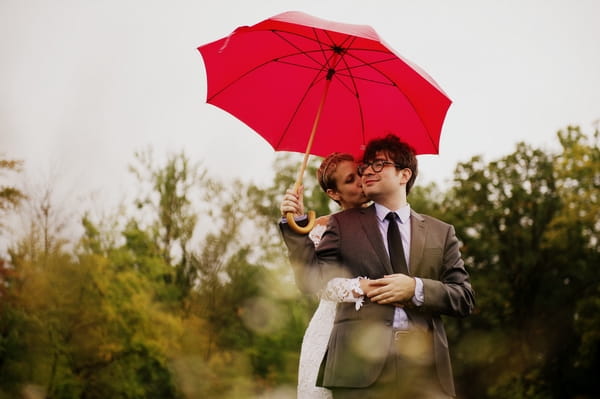 Bride and groom kissing under red umbrella - Picture by Judy Pak Photography