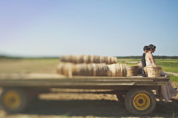 Bride and groom sitting on the back of a trailer - Picture by Our Labor of Love Photography