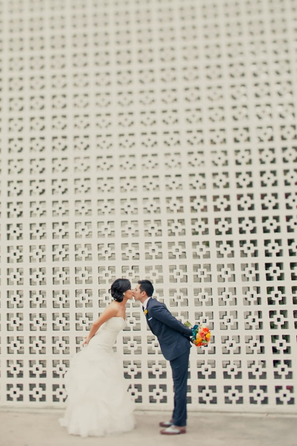 Bride and groom kissing in front of large patterned wall - Picture by onelove photography