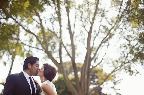 Bride and groom kissing in front of tree branches - Picture by Joielala