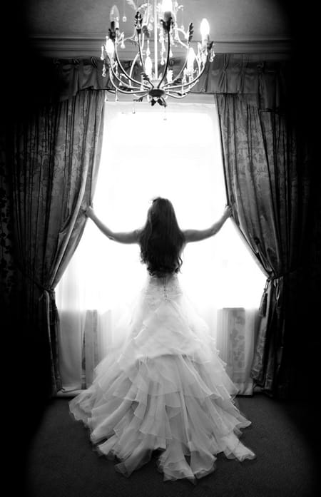 Black and white picture of bride opening curtains in front of window - Picture by Karli Harrison Photography