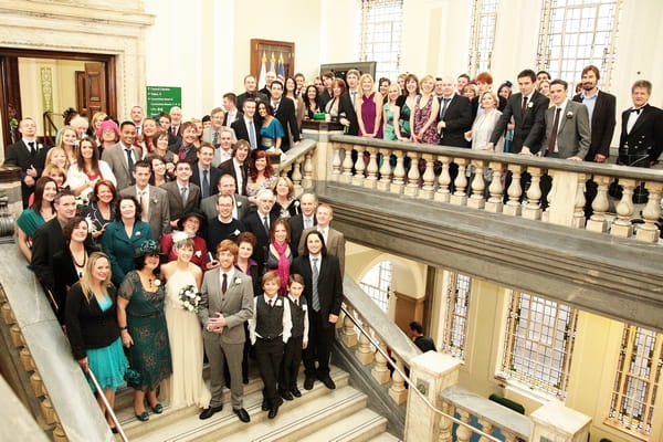 Wedding guests pose for group shot on balcony and staircase - Picture by Rebecca Prigmore Photography