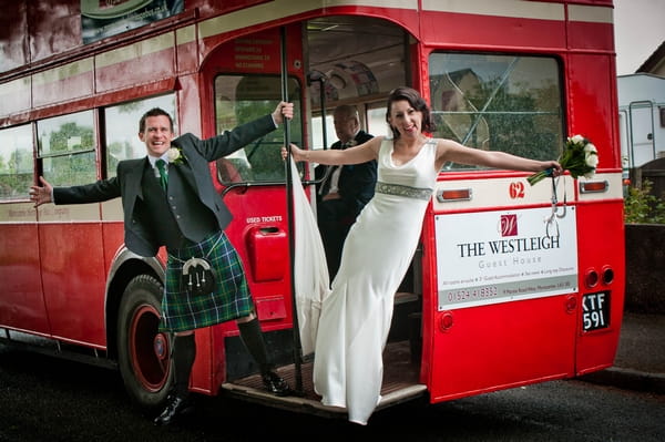 Bride and groom hanging off back of red bus - Picture by Jonathan Bean Photography