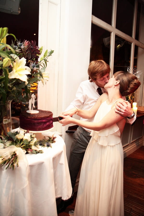 Bride and groom kiss as they cut wedding cake - Picture by Rebecca Prigmore Photography