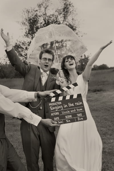 Bride and groom posing with umbrella behind movie clapperboard - A Homemade Marquee Wedding