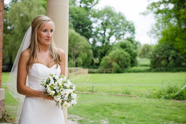 Bride standing next to pillar holding bouquet - A Beautiful Garden Party Wedding at Lains Barn