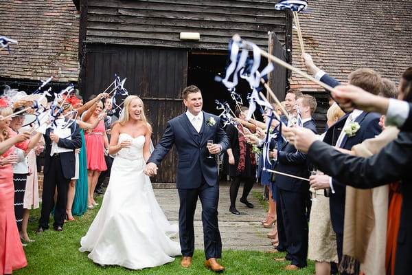 Bride and groom walking past guests with confetti wands - A Beautiful Garden Party Wedding at Lains Barn