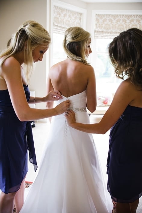 Bridesmaids doing up bride's dress - A Beautiful Garden Party Wedding at Lains Barn