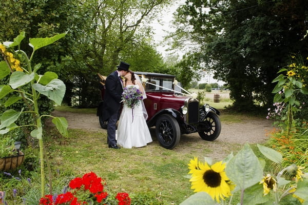 Bride and groom kissing by vintage wedding car