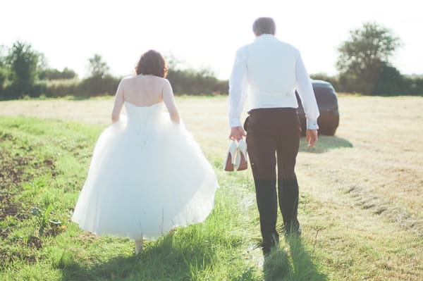 Bride and groom walking across field - A Farm Wedding with a British Summer Theme