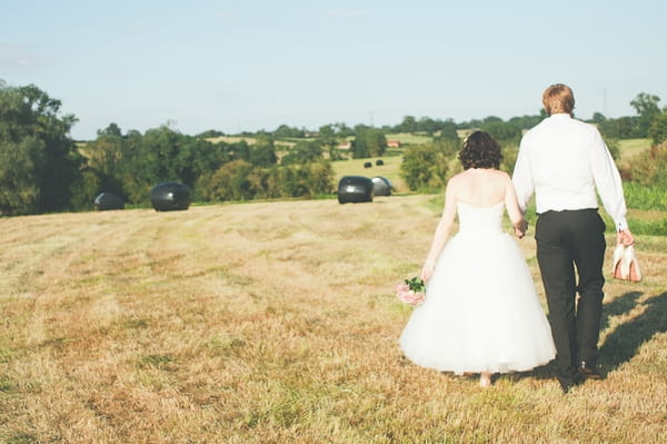 Bride and groom walking across field at Winkworth Farm - A Farm Wedding with a British Summer Theme