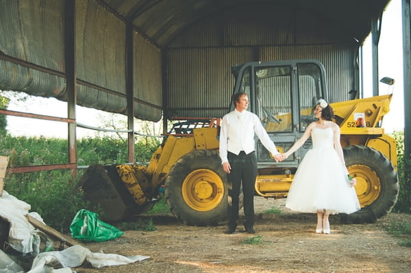 Bride and groom holding hands in front of a tractor - A Farm Wedding with a British Summer Theme