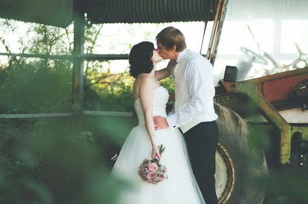 Bride and groom kiss next to tractor - A Farm Wedding with a British Summer Theme