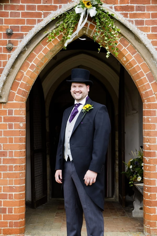 Groom in top hat standing outside church