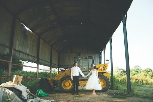 Bride and groom holding hands in front of a tractor - A Farm Wedding with a British Summer Theme