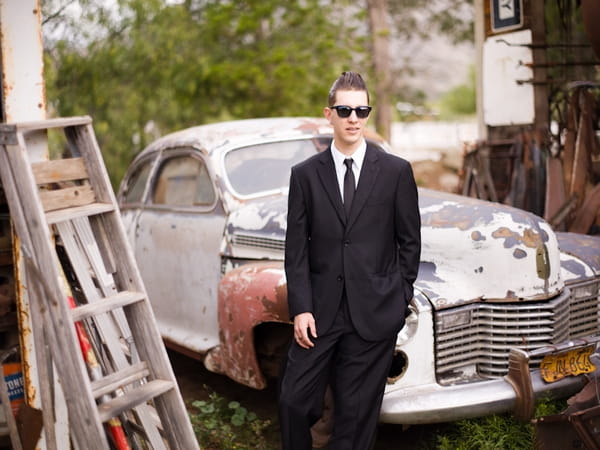 Groom standing in front of old car