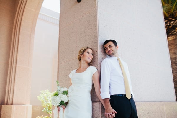 Bride and groom leaning back on pillar