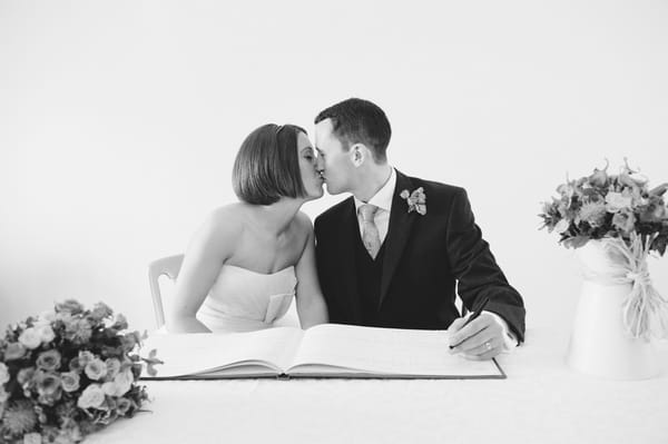 Bride and groom kissing whilst signing the register - Picture by Aaron Collett Photography