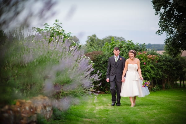 Bride and groom walking hand in hand through garden - Picture by Aaron Collett Photography