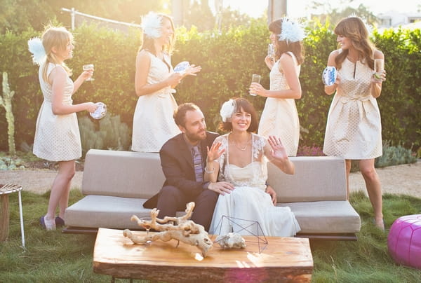 Bride and groom sitting on sofa with bridesmaids behind them