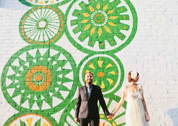 Bride and groom holding hands in front of green wall art