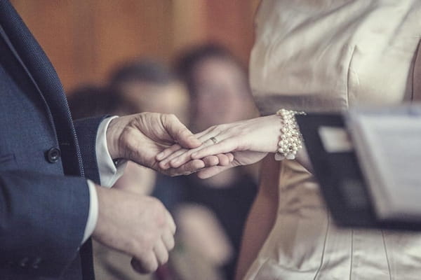 Groom holding bride's hand to put ring on finger