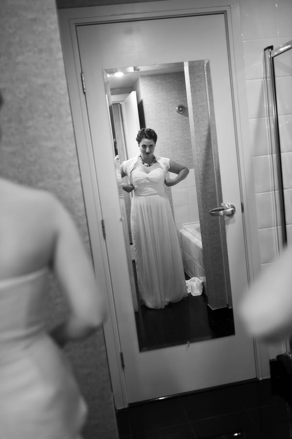 Bride putting on dress looking in the mirror
