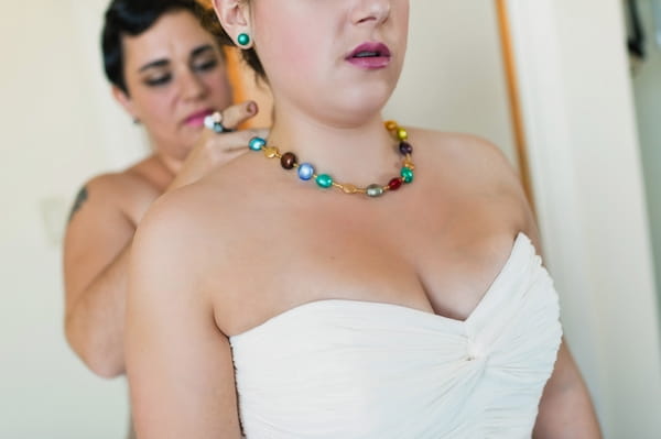 Bridesmaid putting on bride's necklace