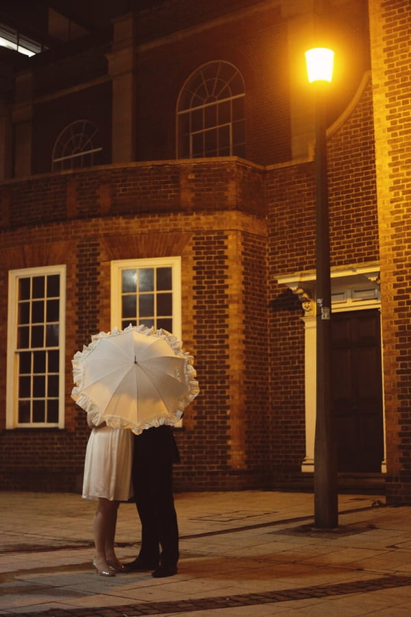 Bride and groom hiding behind umbrella