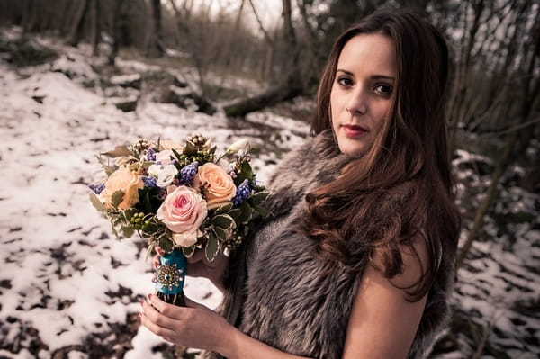 Bride wearing fur shrug, holding bouquet in woods