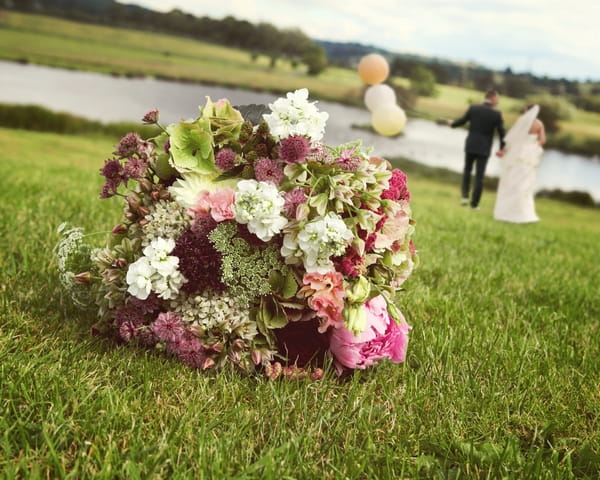 Bridal bouquet on grass with bride and groom in background